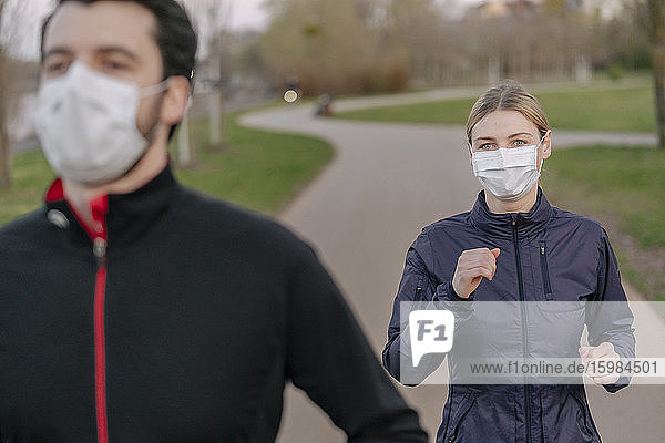 Junger Mann und Frau mit Gesichtsmaske beim Joggen auf dem Fußweg im Park während COVID-19