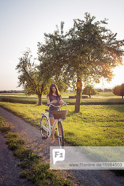 Teenager-Mädchen steht neben Fahrrad auf unbefestigten Weg bei Sonnenuntergang