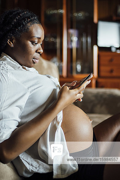 Pregnant young woman using cell phone on couch
