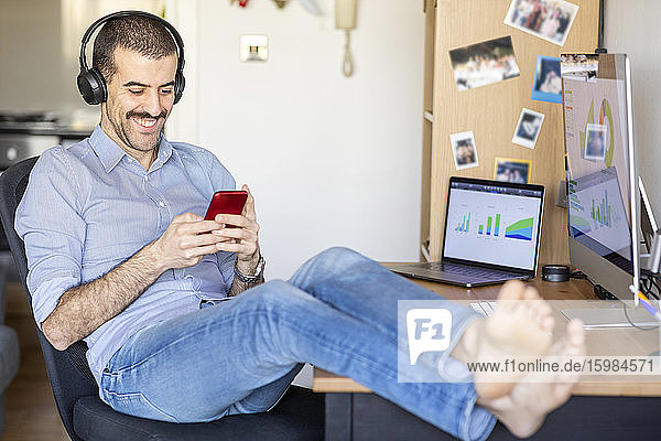Mann arbeitet von zu Hause aus  macht eine Pause  benutzt Smartphone mit Kopfhörern