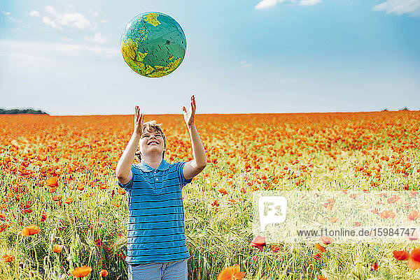 Happy boy catching globe while standing in poppy field against sky on sunny day