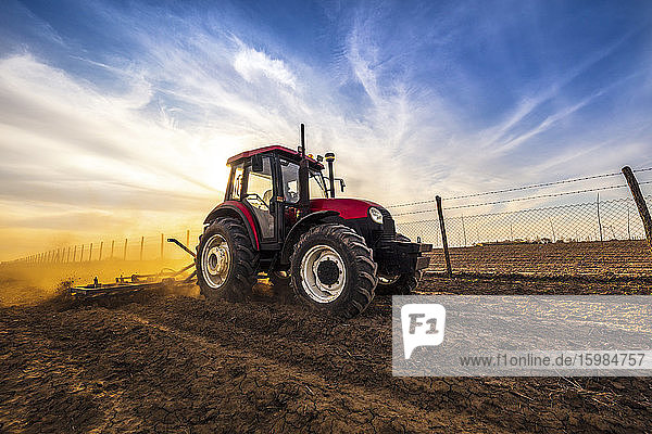 Mann in Traktor pflügt landwirtschaftliche Flächen gegen bewölkten Himmel