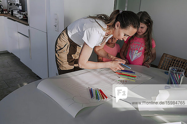 Mutter  die ihren Töchtern beim Zeichnen auf Papier zu Hause hilft