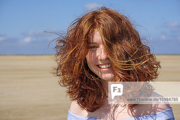 Close-up-Porträt von sorglos Rothaarige Teenager-Mädchen stehen am Strand gegen den Himmel auf sonnigen Tag