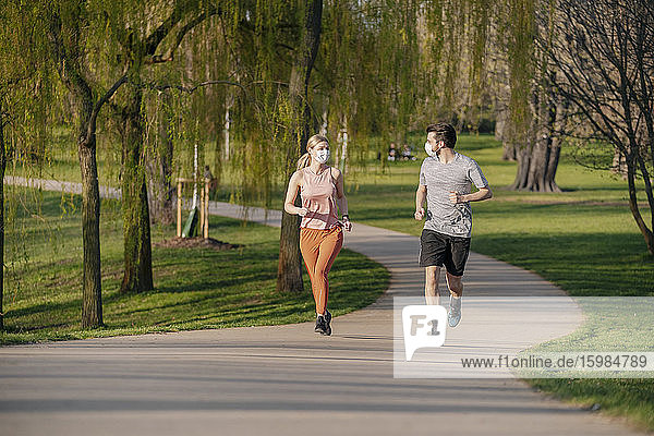 Couple wearing face masks while running on footpath at park