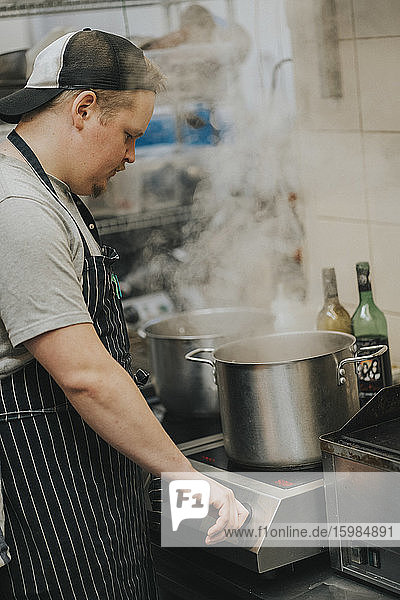 Young male chef cooking food in pot at restaurant kitchen