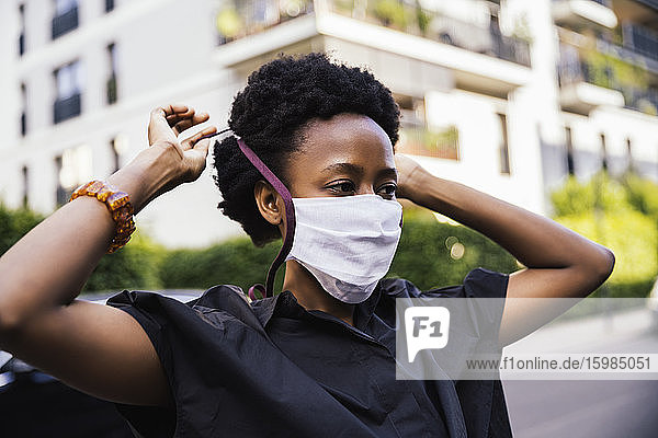 Portrait of young woman putting on protective mask outdoors