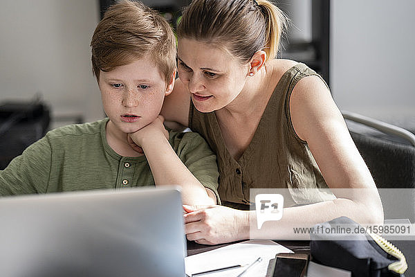 Mother homeschooling her son and using laptop at home