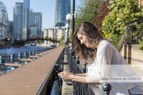 Young woman using smartphone leaning on railing of promenade