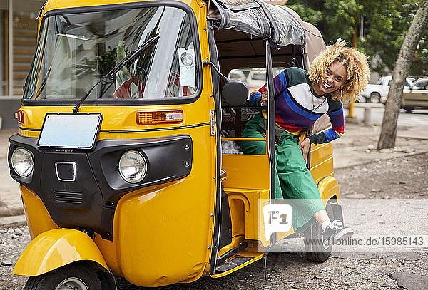 Full length portrait of smiling young woman leaning out from tuk-tuk in city