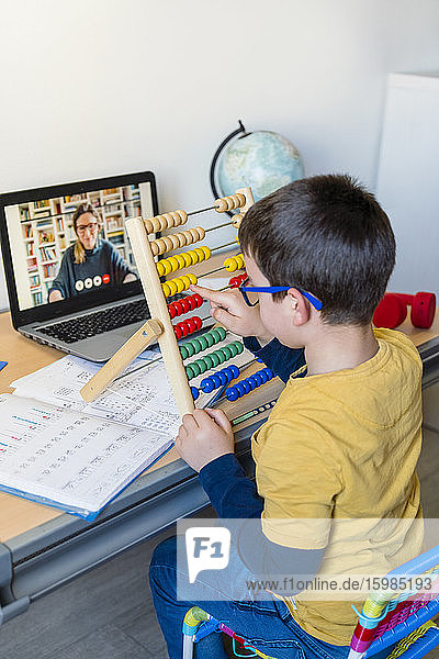 Elementary student using abacus with teacher on video call during homeschooling