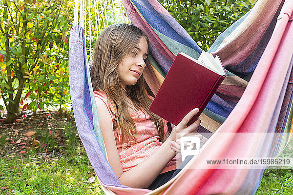 Porträt eines Mädchens  das in der Hängematte ein Buch liest