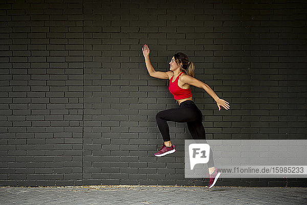 Mittlere erwachsene Frau in Sportkleidung beim Laufen gegen eine Mauer