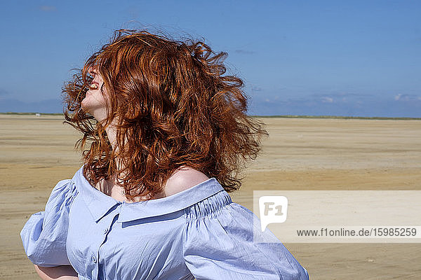 Unbekümmertes Teenager-Mädchen mit zerzausten Haaren am Strand stehend gegen den Himmel an einem sonnigen Tag