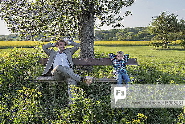 Relaxed man sitting with son on bench at park