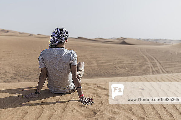 Young man sitting on sand dunes in desert at Dubai  United Arab Emirates