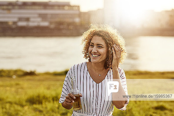 Portrait of smiling woman with glass bottle at riverside