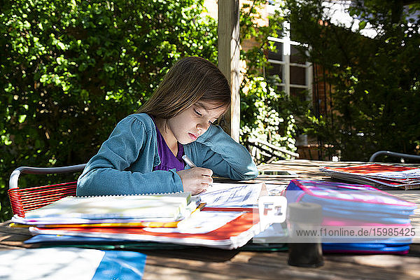 Girl sitting at garden table doing homework