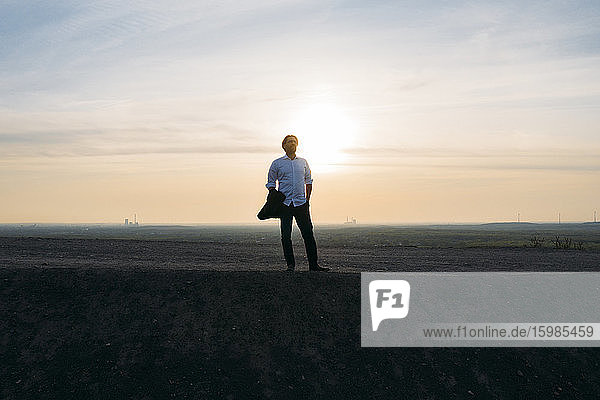 Männlicher Unternehmer steht auf einem Hügel gegen den Himmel bei Sonnenuntergang