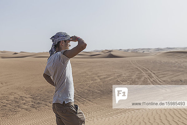 Männlicher Tourist  der seine Augen abschirmt  während er auf Sanddünen in der Wüste von Dubai  Vereinigte Arabische Emirate  steht