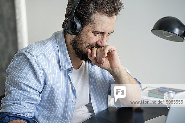 Mann mit Laptop und Kopfhörern bei der Arbeit zu Hause