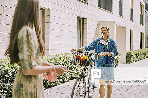 Zwei Frauen mit Fahrrad und Gesichtsmaske treffen sich in einem städtischen Gebiet