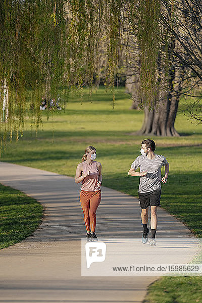 Paar trägt Gesichtsmasken beim Joggen auf dem Fußweg im Park