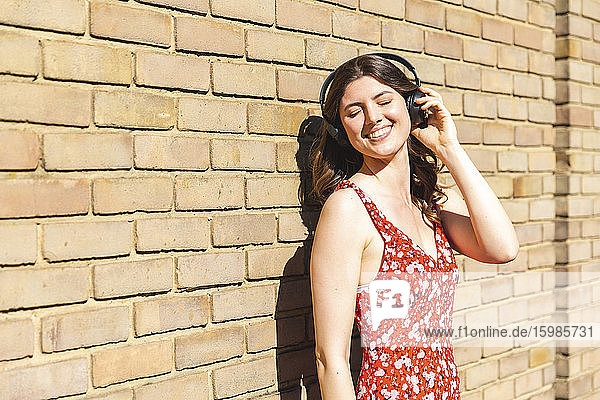 Glückliche junge Frau  die Musik hört und sich an eine Mauer lehnt