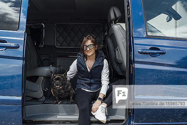 Porträt einer lächelnden Frau  die mit ihrer Bulldogge in einem Lieferwagen sitzt