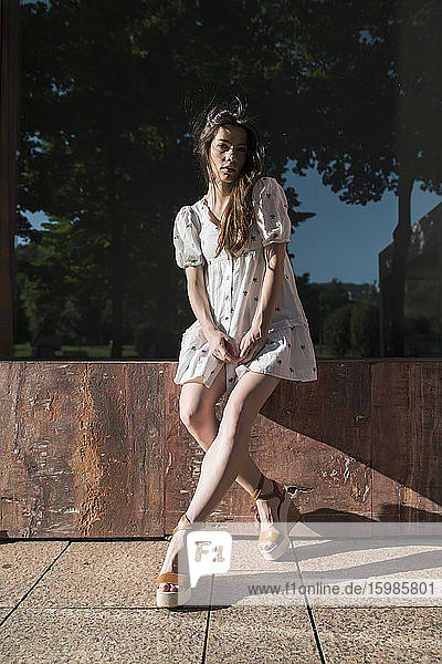 Schöne junge Frau im Minikleid sitzt auf einer Holzplanke während eines sonnigen Tages