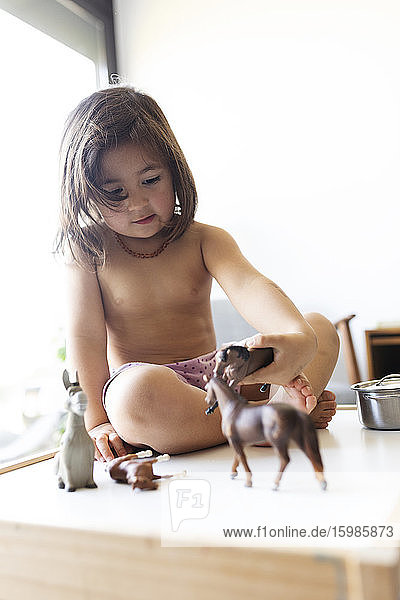 Porträt eines kleinen Mädchens ohne Hemd  das mit Spielzeugpferden spielt