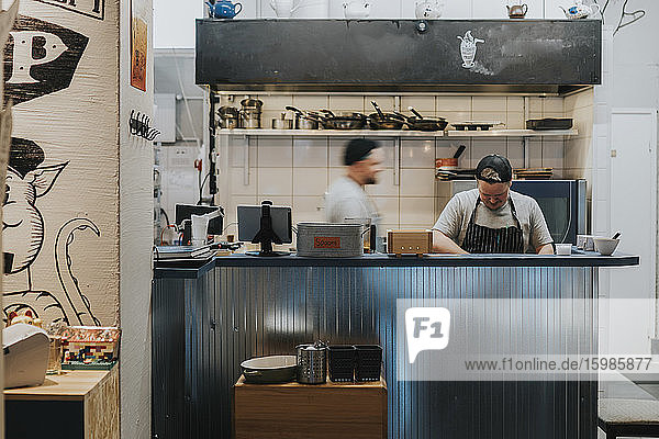 Männliche Köche bei der Zubereitung von Speisen hinter dem Tresen in einer beleuchteten Restaurantküche