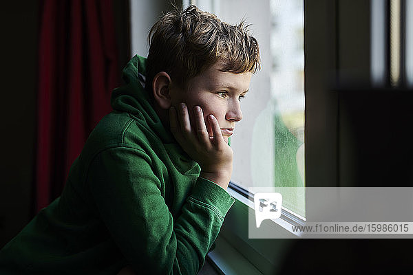 Gelangweilter Junge schaut zu Hause aus dem Fenster