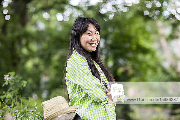 Smiling woman with pruner in urban garden