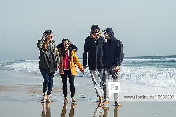 Freunde unterhalten sich in voller Länge beim Spaziergang am Strand gegen den Himmel in Tarifa  Spanien