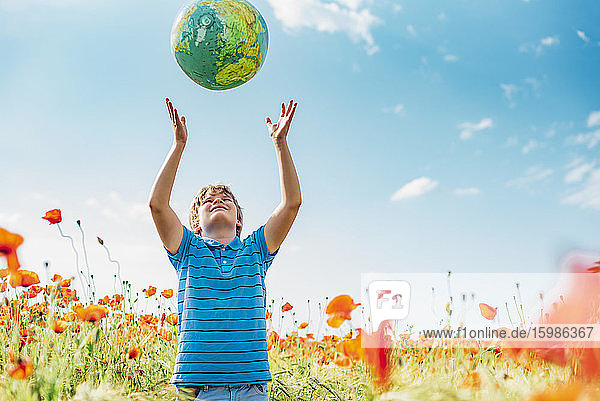 Boy catching globe while standing in poppy field against sky on sunny day