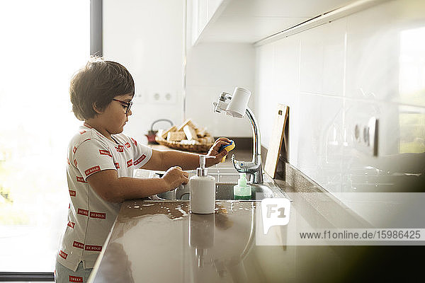 Junge wäscht zu Hause Geschirr