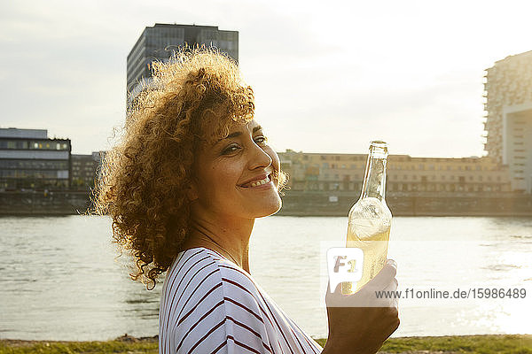 Portrait of smiling woman with glass bottle at riverside