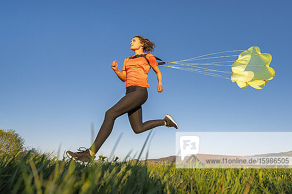 Low angle view of young woman sprinting with parachute against clear blue sky