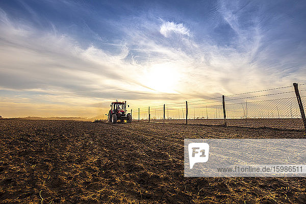 Farmer in tractor plowing agricultural land against cloudy sky