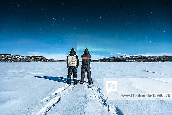 Snowshoe hikers standing in winter landscape watching northern lights above Ropijarvi  Ropinsalmi  Enontekioe  Finland