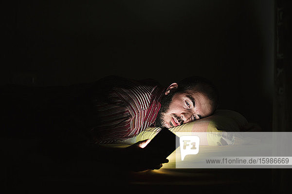 Mann liegt im Bett und benutzt nachts sein Smartphone