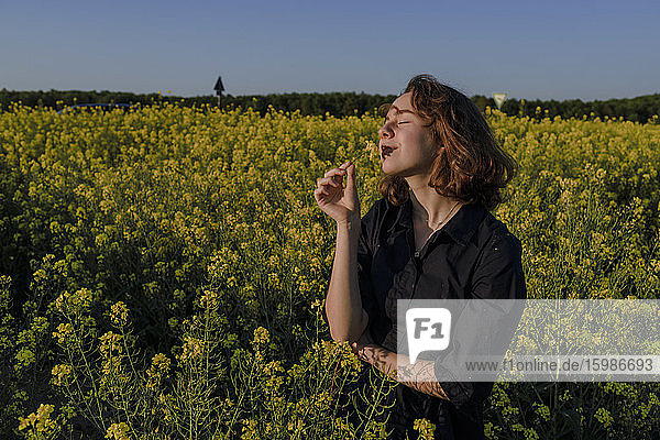Porträt eines glücklichen Teenager-Mädchens mit geschlossenen Augen  das im Rapsfeld steht