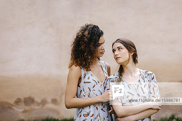 Verliebte Schwestern in Kleidern  die sich gegenseitig anschauen  während sie an einer alten Wand stehen