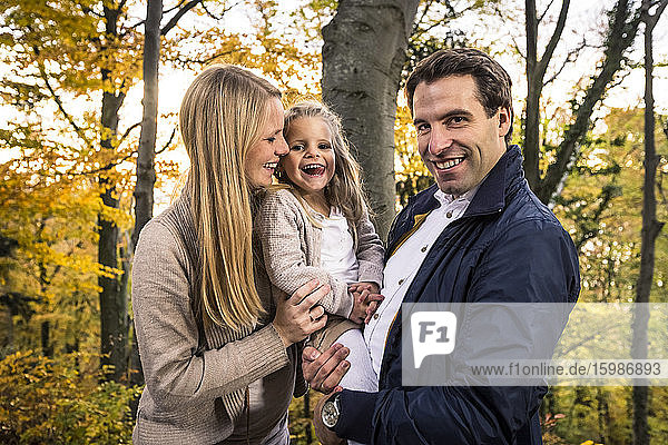 Lächelnder Mann  der seine Tochter trägt  während er neben einer schwangeren Frau im Wald steht