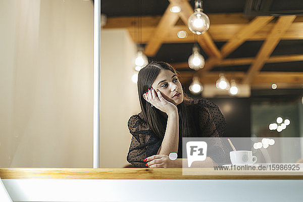 Nachdenkliche junge Frau sitzt am Tisch in einem beleuchteten Café