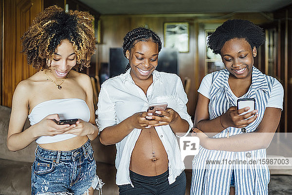 Schwangere junge Frau  junge Frau und Teenager-Mädchen  die zu Hause ein Mobiltelefon benutzen