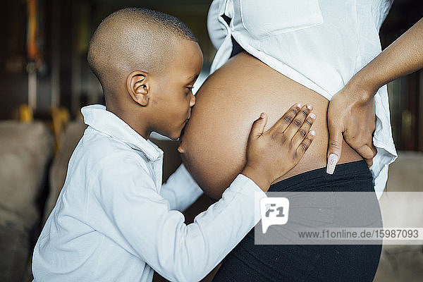 Kleiner Junge küsst den Bauch einer schwangeren jungen Frau