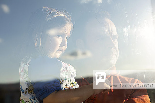 Porträt von Vater und kleiner Tochter hinter einer Fensterscheibe mit Blick in die Ferne