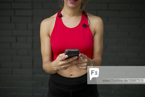 Weibliche Sportlerin in Sportkleidung  die ein Smartphone benutzt  während sie an der Wand steht